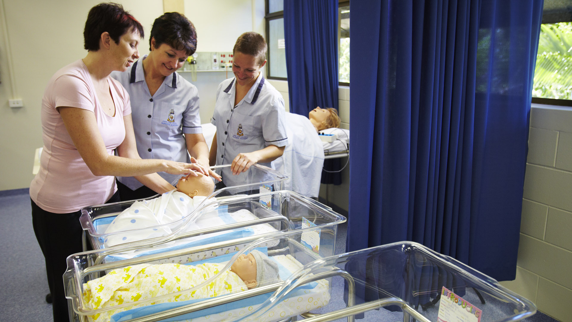 JCU Midwifery lecturers and students stand next to a row of newborn hospital beds. 