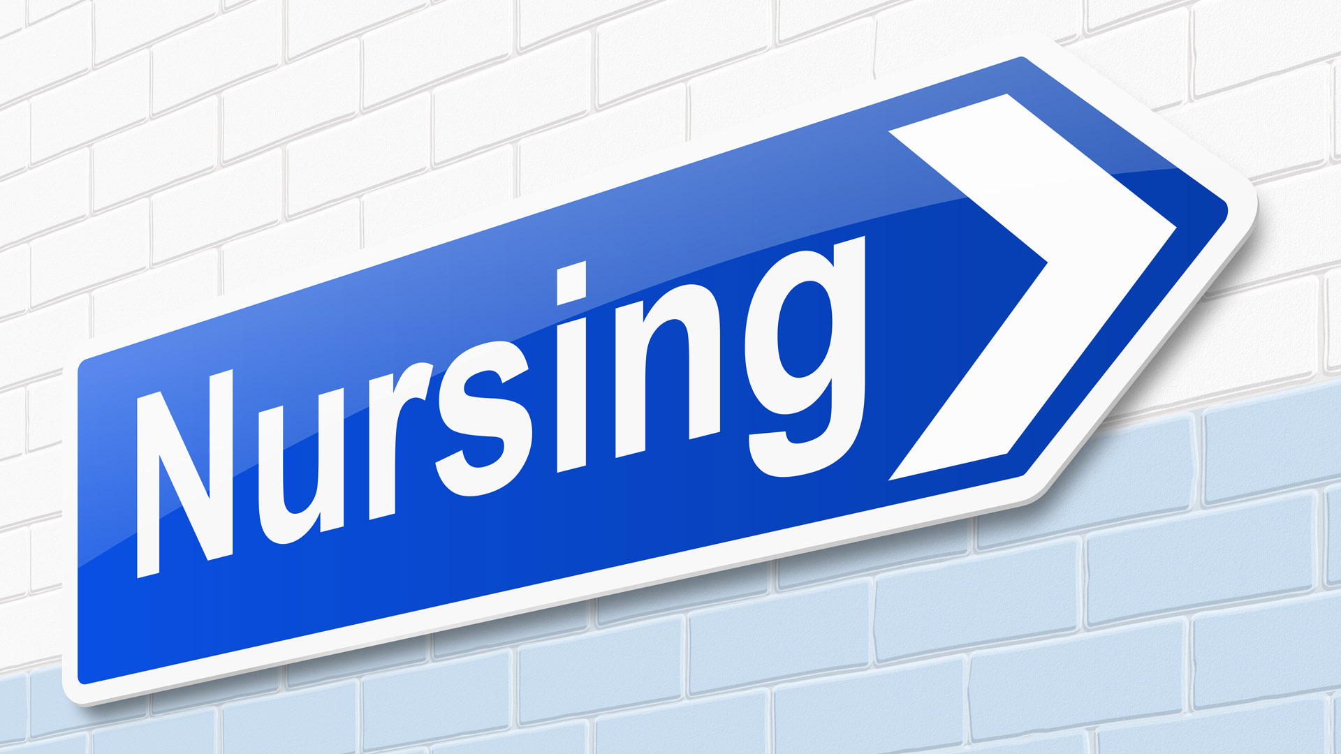 A blue arrow sign with the word Nursing on it points to the right and is affixed to a brick wall. 