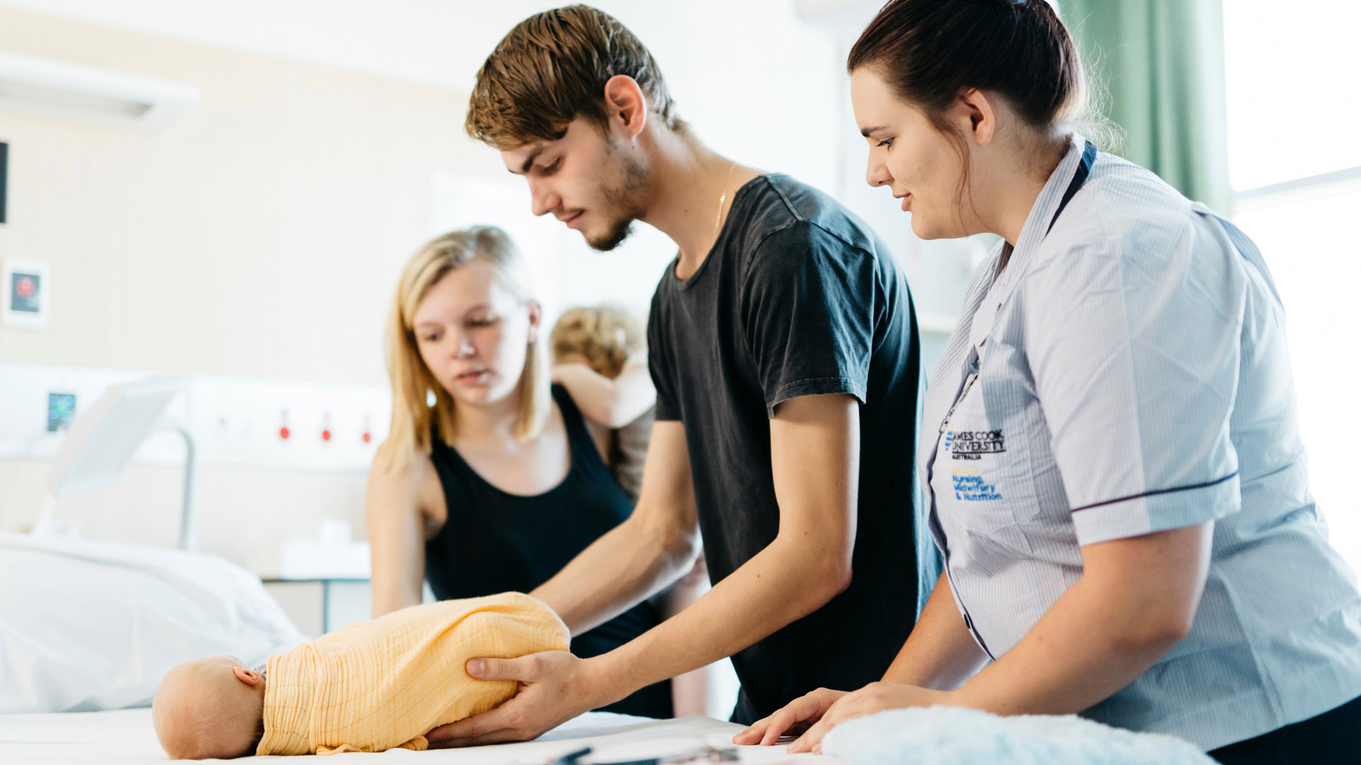 A JCU Midwifery student works with parents and their newborn on swaddling techniques. 