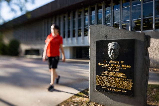 A student wearing a red shirt is out of focus as she walks past the Eddie Koiki Mabo commemorative plaque