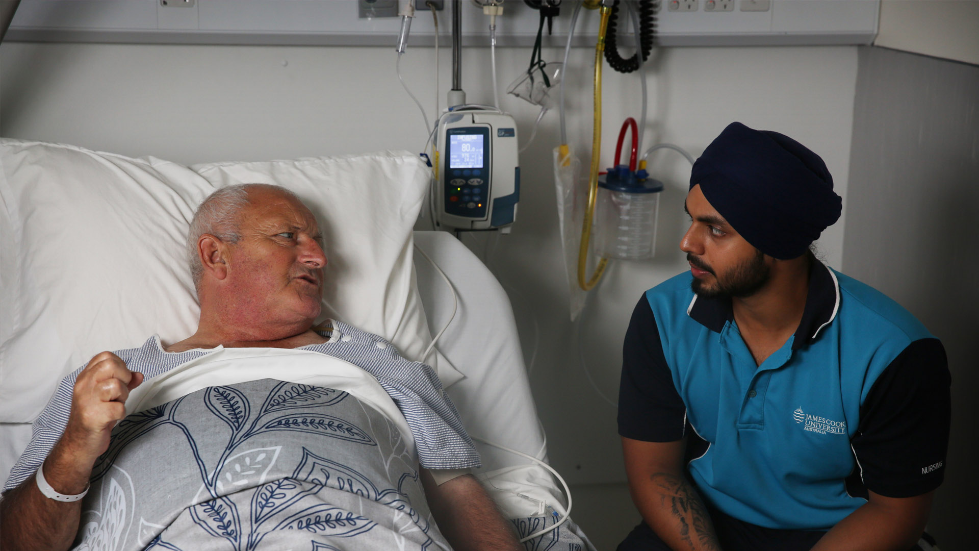 A James Cook University nursing student sits at the bedside of an elderly male patient. 