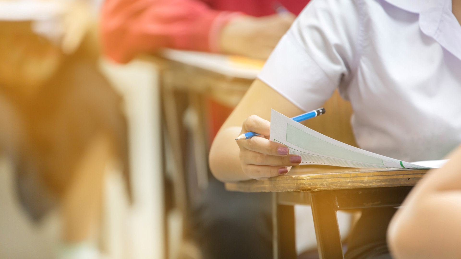 Students sit at wooden desks completing an assessment. 