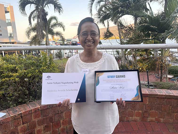 PhD candidate Antin Widi smiling while holding two award certificates