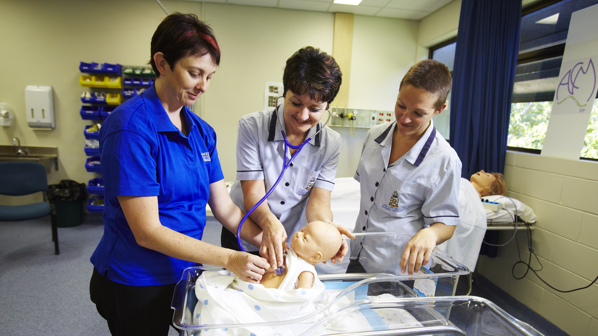 Three James Cook University Nursing and Midwifery students examine an anatomic model of an infant with a stethoscope. 