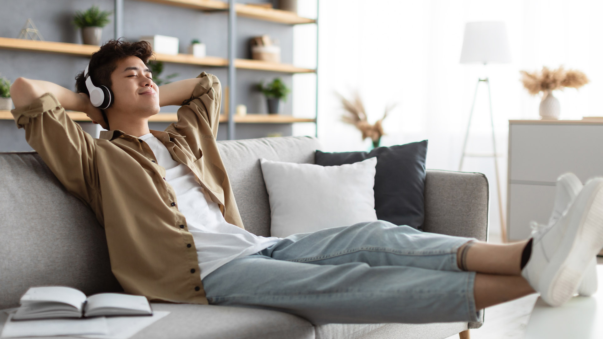 A student sits in a relaxed position on a couch, with his hands behind his head, his eyes shut and his feet on the coffee table. 